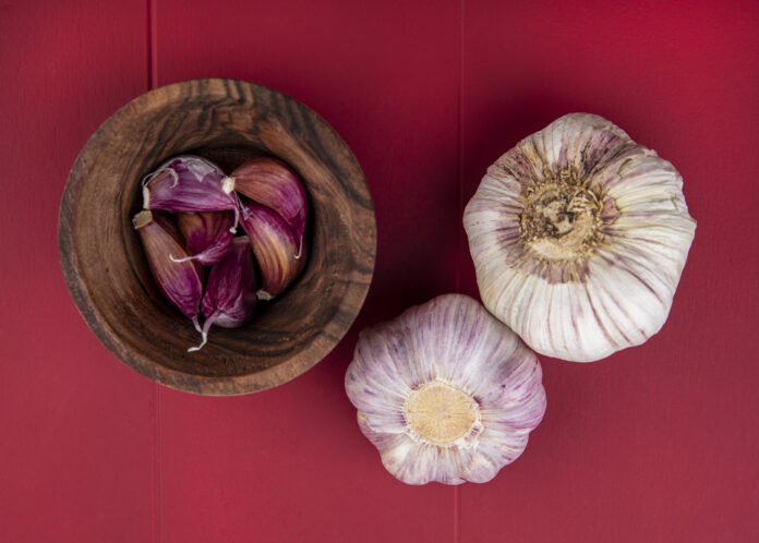 top view of garlic cloves in bowl and garlic bulbs on red background